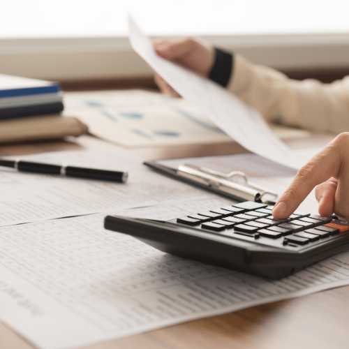 A close-up of a person's hand typing on a calculator and holding a piece of paper